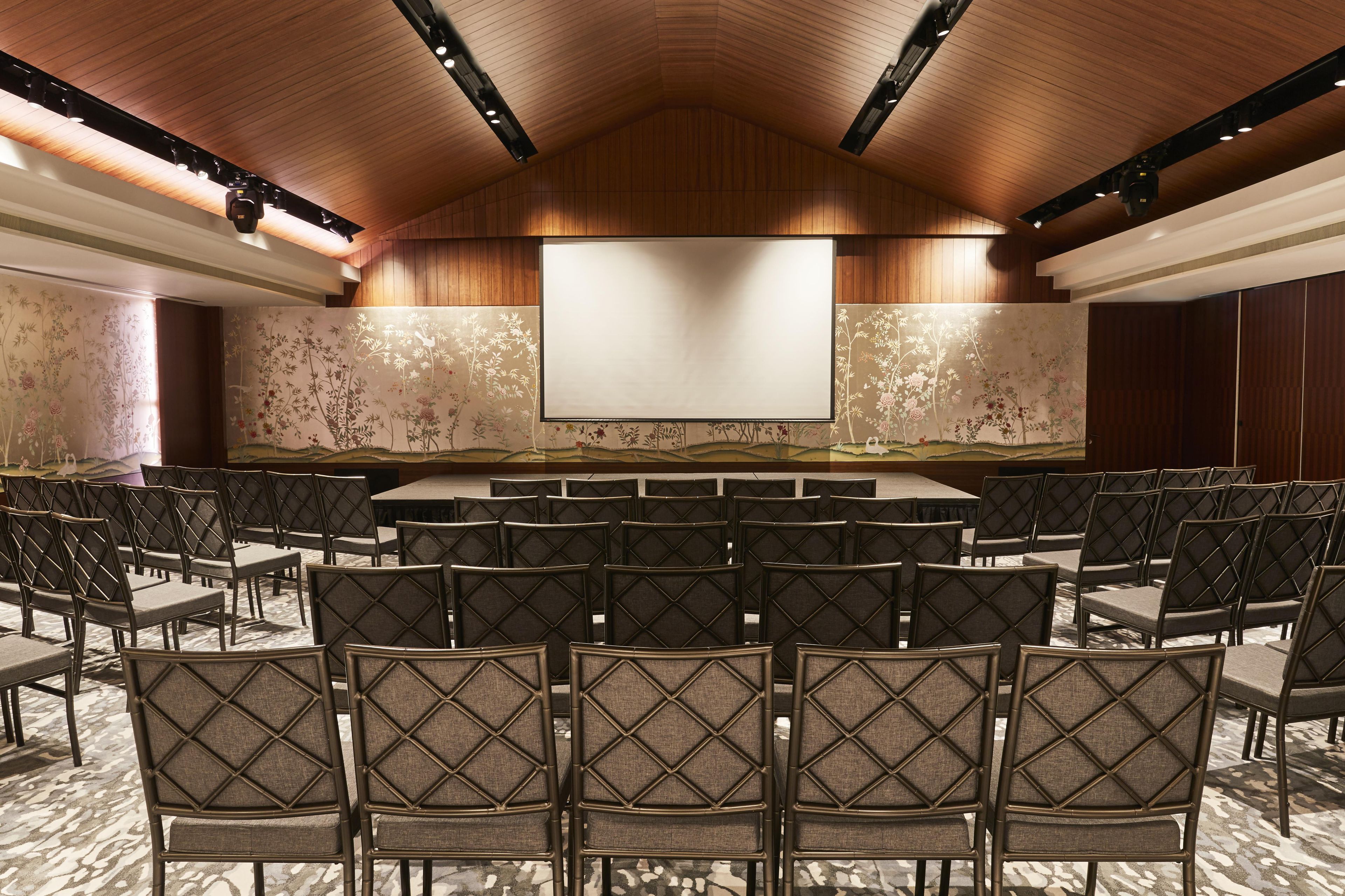 A conference room with a large screen, rows of chairs, and a wooden ceiling.