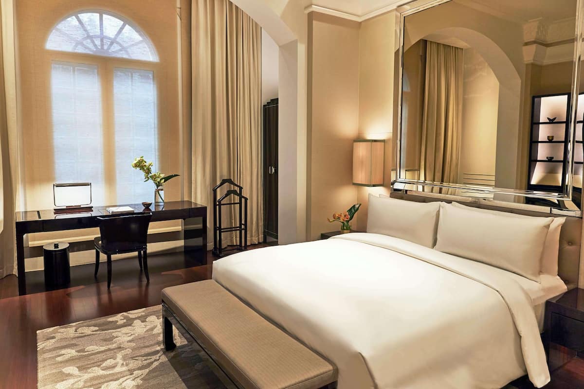 A hotel room with a large bed, a desk with a chair, a lamp, and a mirror.