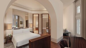 A hotel room with a large bed, a wooden desk, a chair, a mirror, and a view of the outside through a window. - The Capitol Kempinski Hotel Singapore (Singapore)