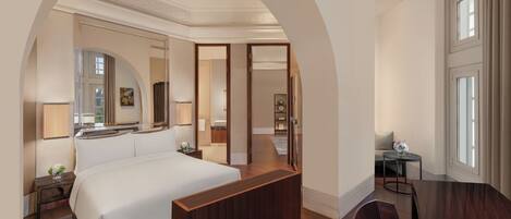 A hotel room with a large bed, a wooden desk, a chair, a mirror, and a view of the outside through a window.