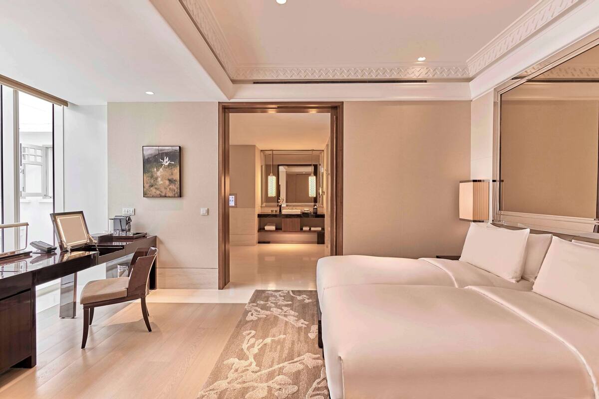 A hotel room with a large bed, a desk with a chair, a desk lamp, a framed picture on the wall, and a mirror above the bed.