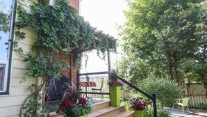 A wooden staircase leading to a porch with a brick wall, a wooden deck, and a green chair. - Danby House (Grey Highlands)