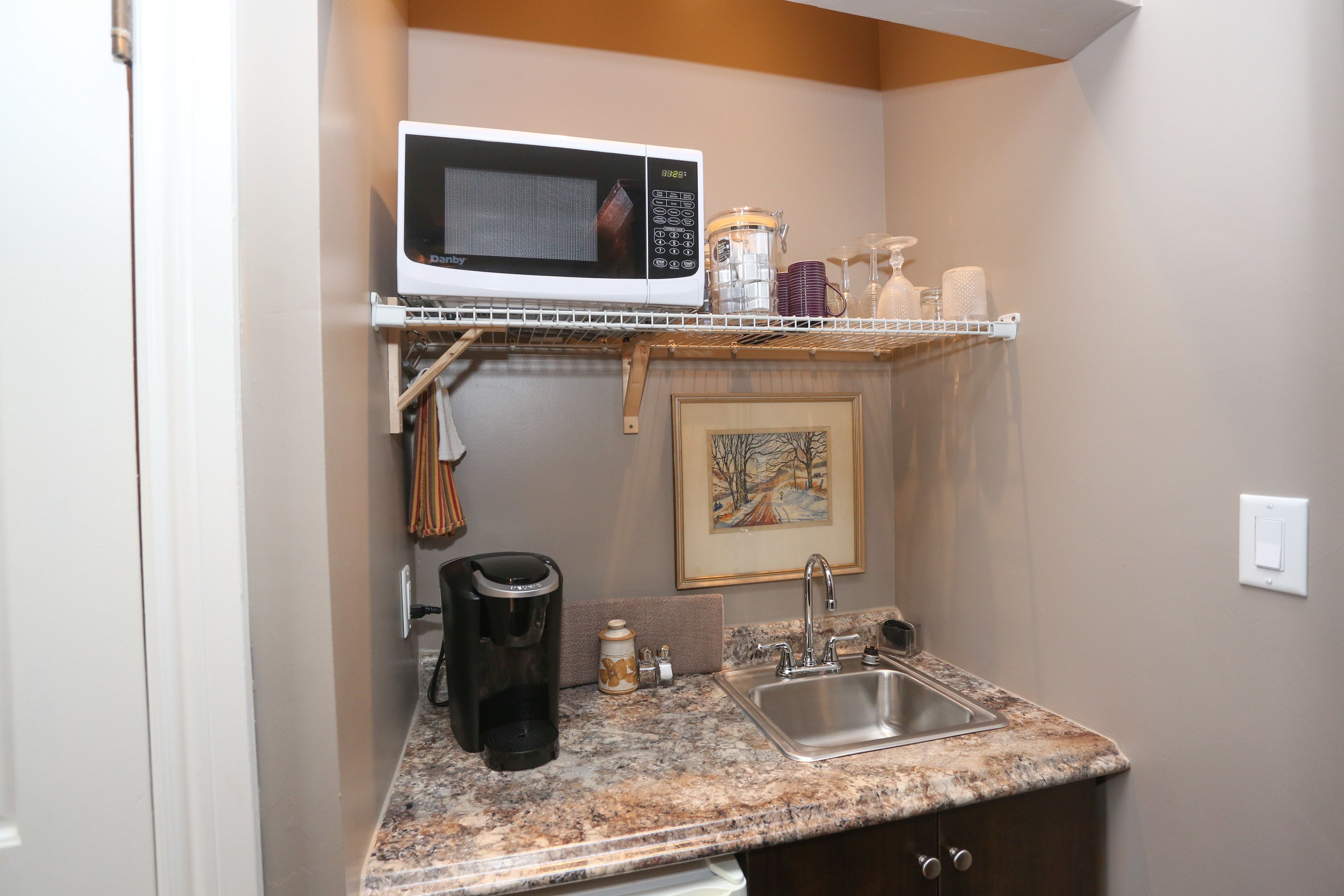 Una cocina compacta con microondas integrado, cafetera y lavamanos.