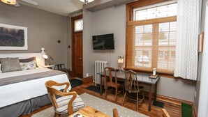 A bedroom with a bed, wooden chairs, a desk, a TV, and a window with blinds. - Danby House (Grey Highlands)