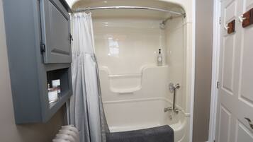 A bathroom with a bathtub, a shower, a towel rack, and a shelf with toiletries.