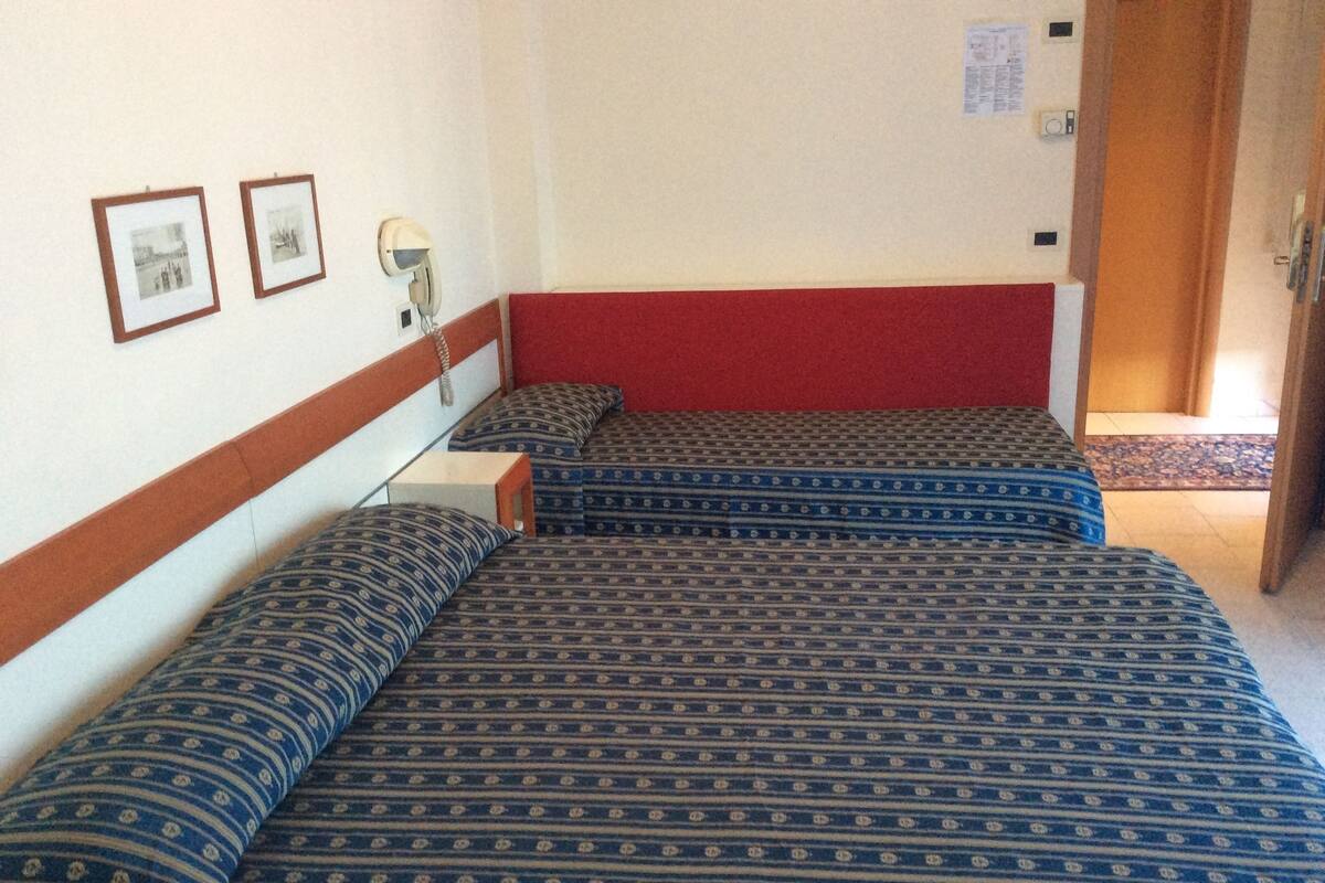 A hotel room with two beds, a red accent wall, a telephone, and framed pictures on the wall.