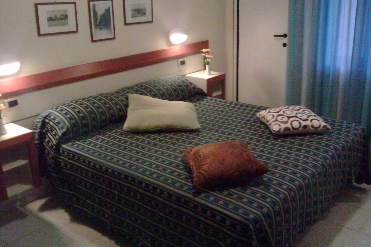 A neatly made bed with patterned bedding, a bedside table with a lamp, and framed pictures on the wall.
