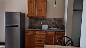 A kitchen with wooden cabinets, a stainless steel refrigerator, a sink, and a dining table with chairs. - Texas Star Lodges (Floresville)