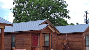 A rustic cabin with a red door, a wooden porch, and a large bull statue. - Texas Star Lodges (Floresville)