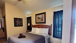 A hotel room with a bed, a ceiling fan, a framed picture, a lamp, and a window with curtains. - Texas Star Lodges (Floresville)