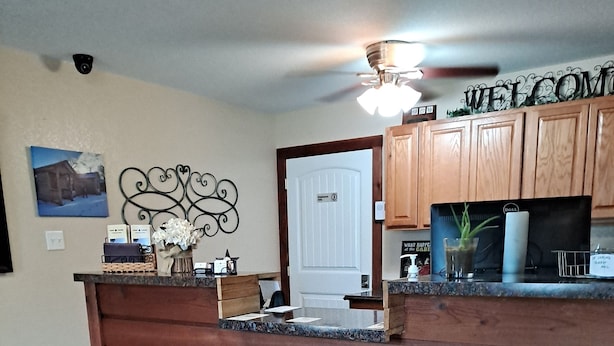 A reception area with a wooden counter, a welcome sign, a desk with a computer, and a door marked "Welcome". - Texas Star Lodges (Floresville)