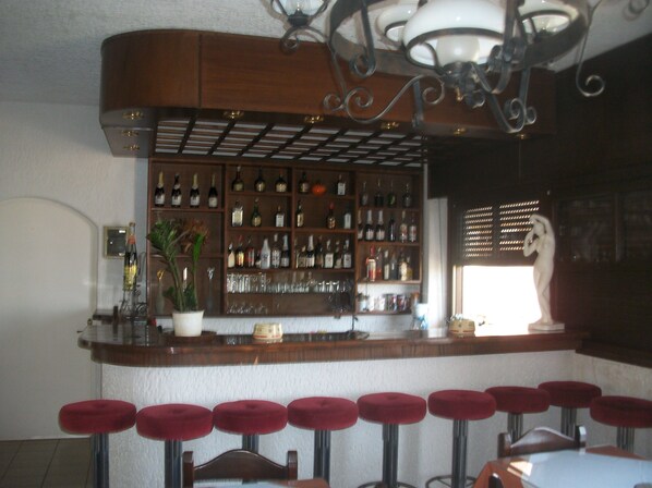 A bar area with a wooden counter, shelves of bottles, glasses, and a statue.