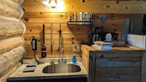 Una cocina acogedora de estilo cabaña, con paredes de madera, un fregadero, una cafetera y una estantería con tazas y vasos.