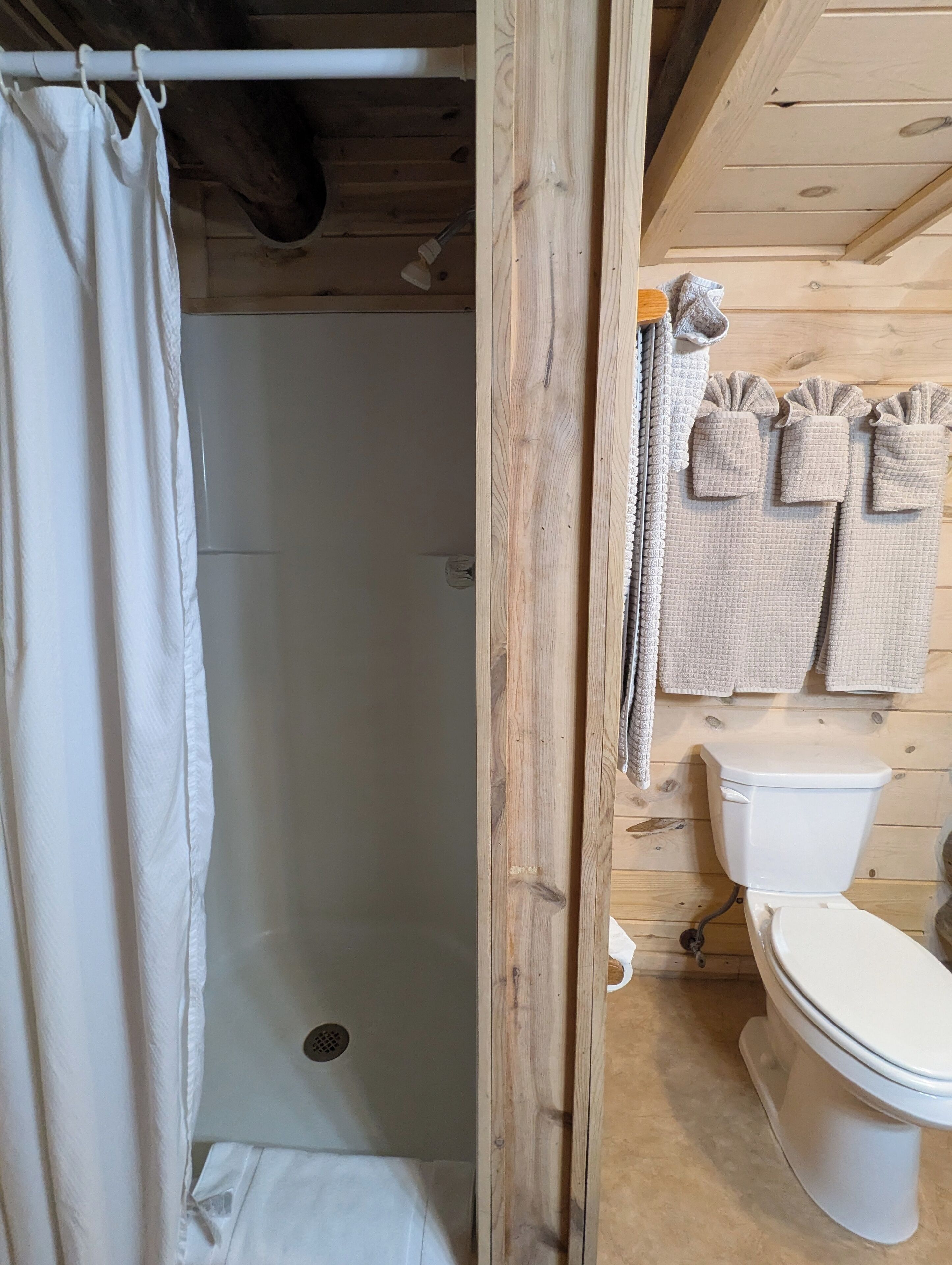 A wooden cabin bathroom with a shower, toilet, and towels hanging on the wall.