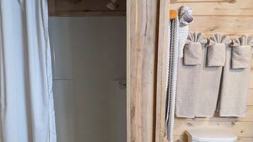 A wooden cabin bathroom with a shower, toilet, and towels hanging on the wall.