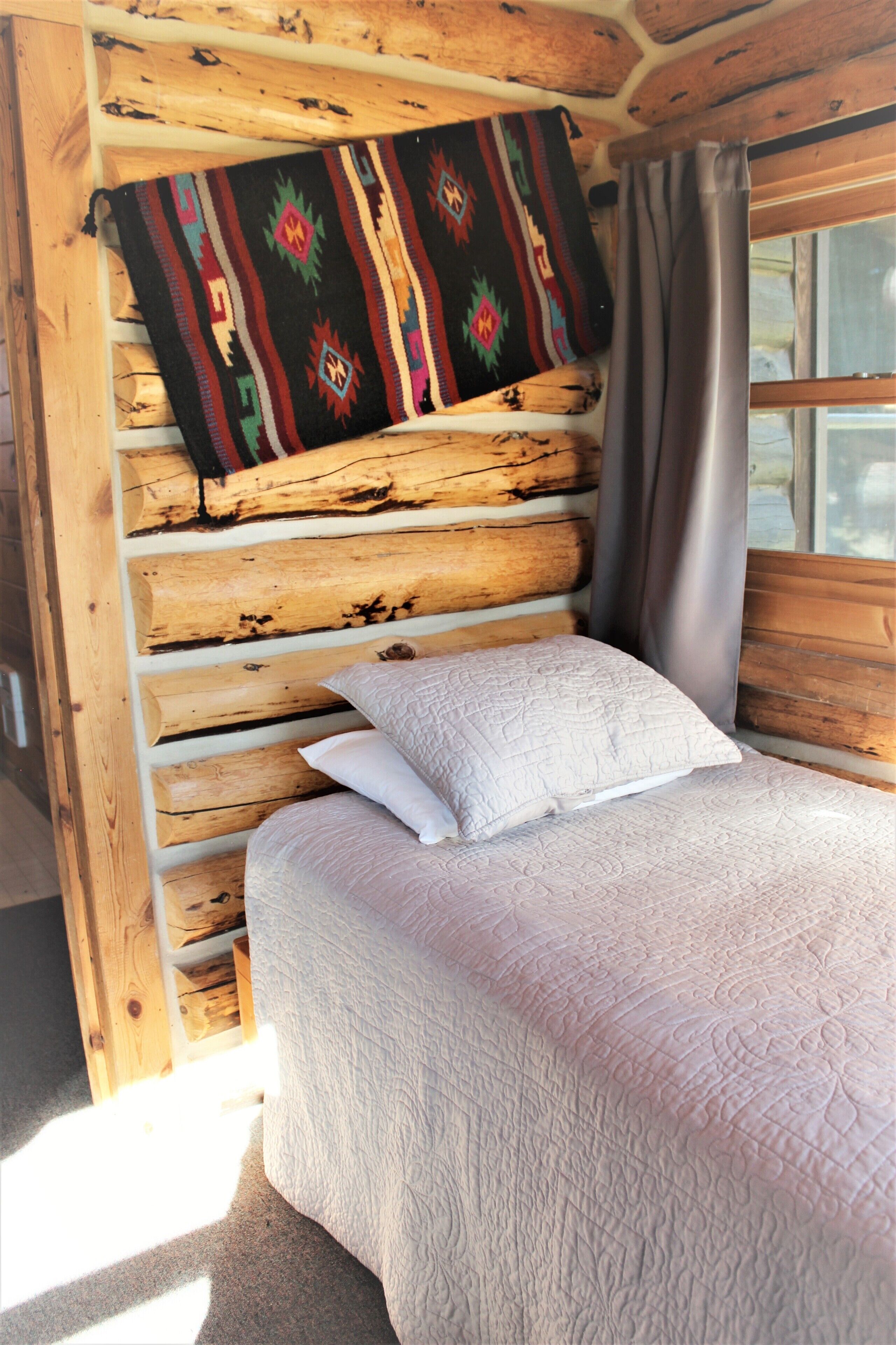 Una habitació de cabana de fusta amb un llit, una manta colorida i una finestra amb cortines.