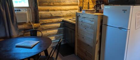 A compact kitchen with a wooden interior, a refrigerator, a microwave, and a small dining table with chairs.