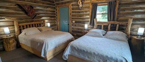 A log cabin bedroom with two wooden beds, a blue door, and a cow skull decoration.