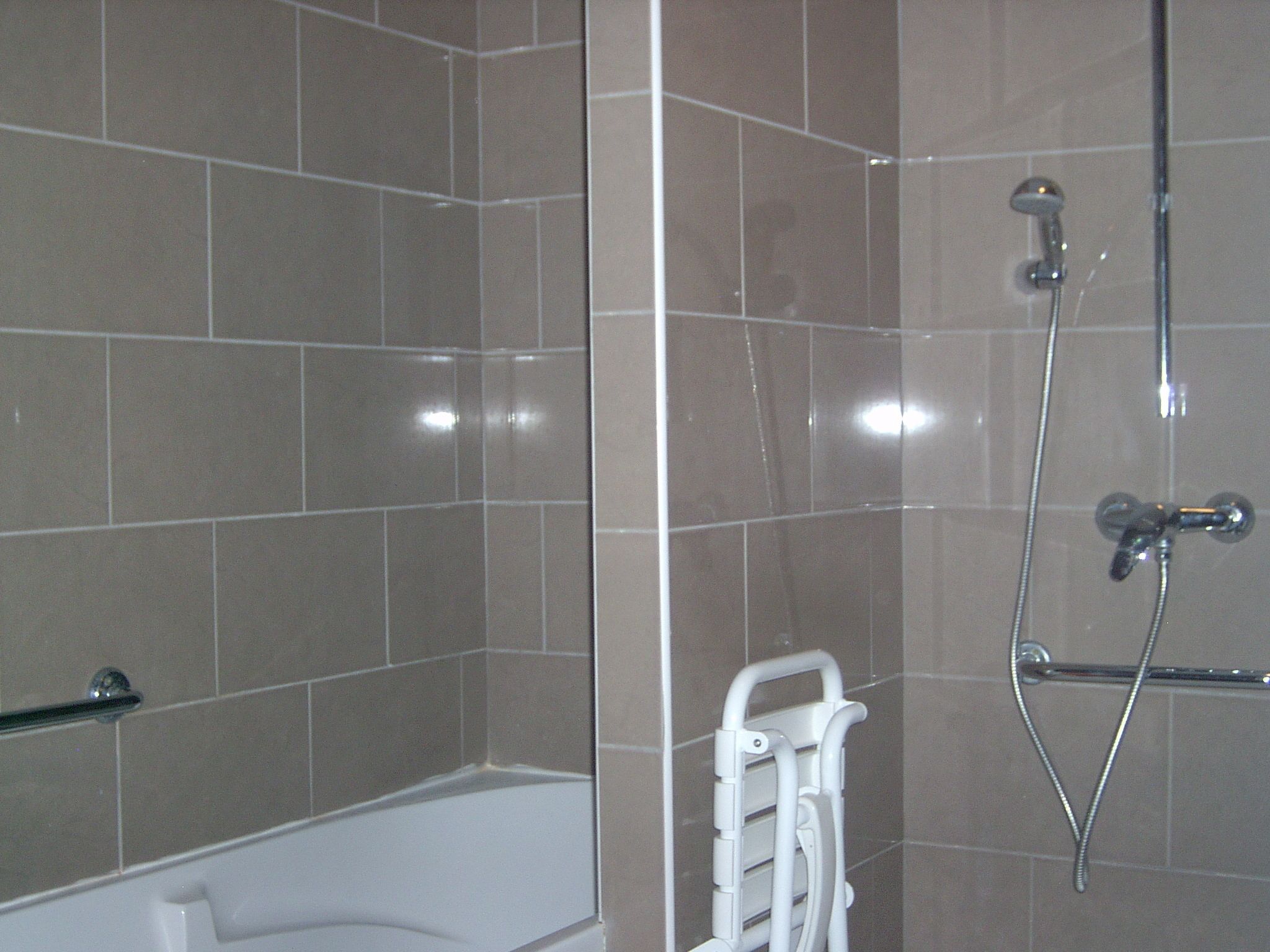 Une salle de bain moderne avec une baignoire, une douche équipée d’un pommeau de douche à main et un porte-serviettes blanc.