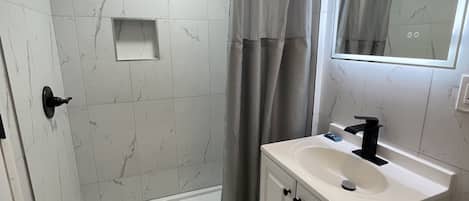 A modern bathroom with a walk-in shower, a vanity with a sink, and a mirror.