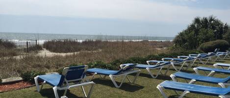 A beachside lounge area with rows of blue and white lounge chairs and a blue table, overlooking the ocean.