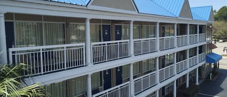A multi-story hotel with balconies, large windows, and a parking area.