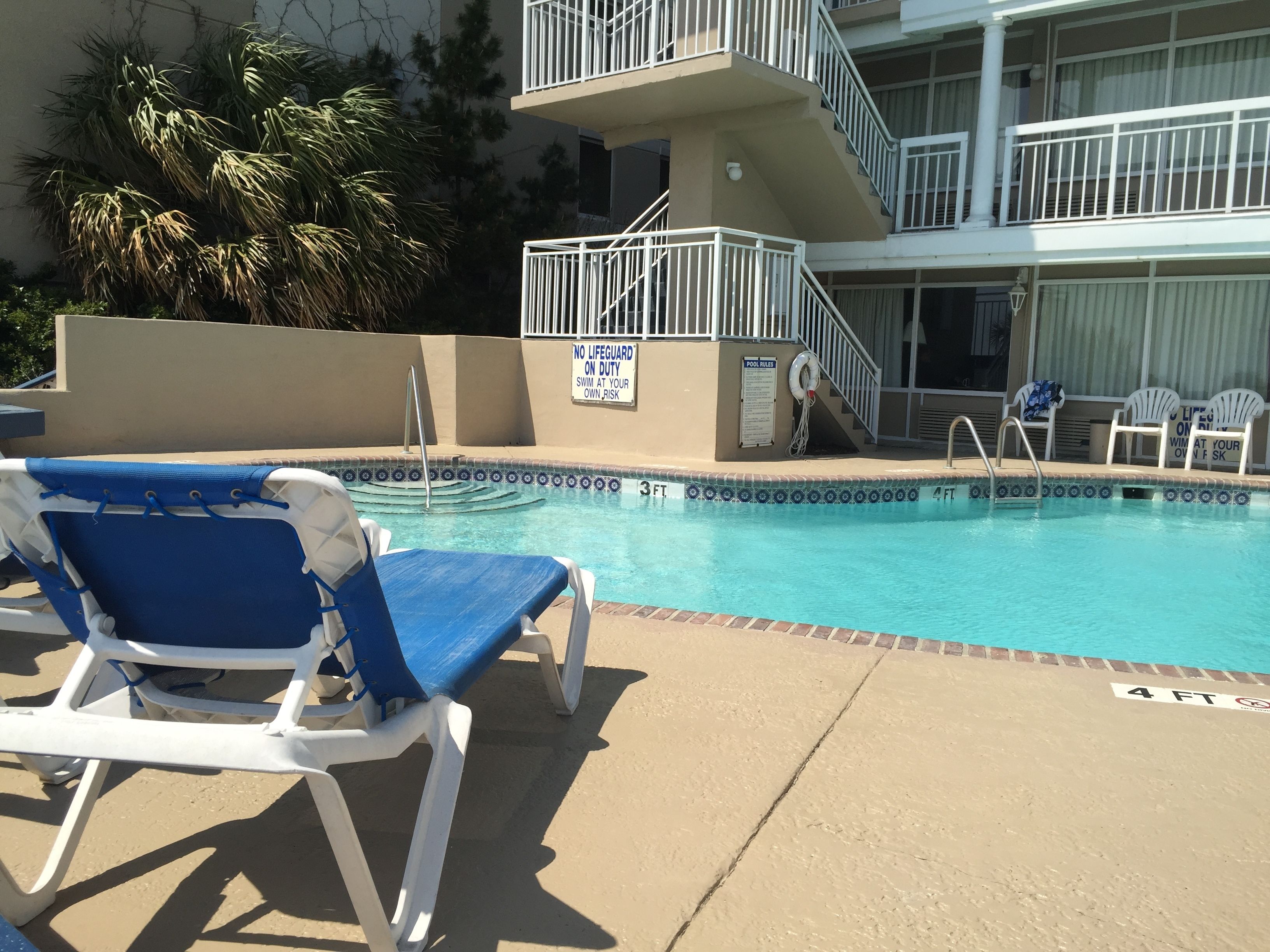 A pool area with lounge chairs, a lifeguard tower, and a sign indicating no lifeguard on duty.