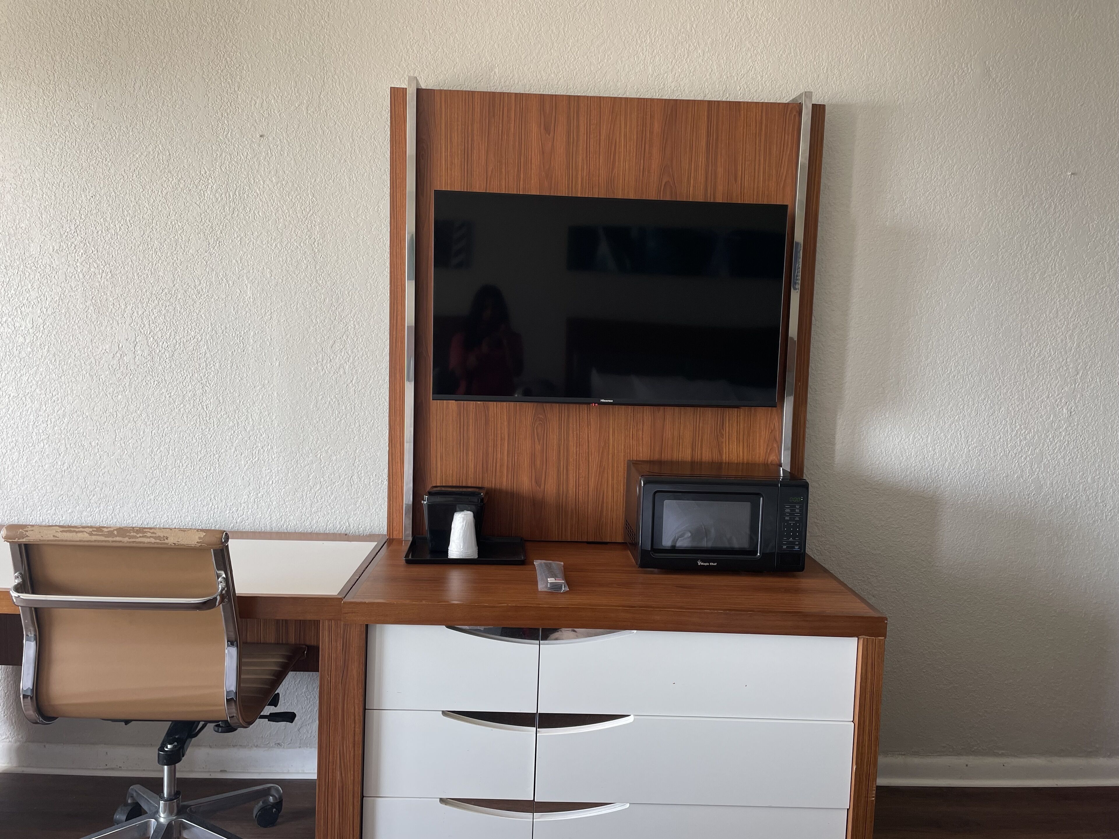 A wooden desk with a built-in TV, a microwave, and a chair.