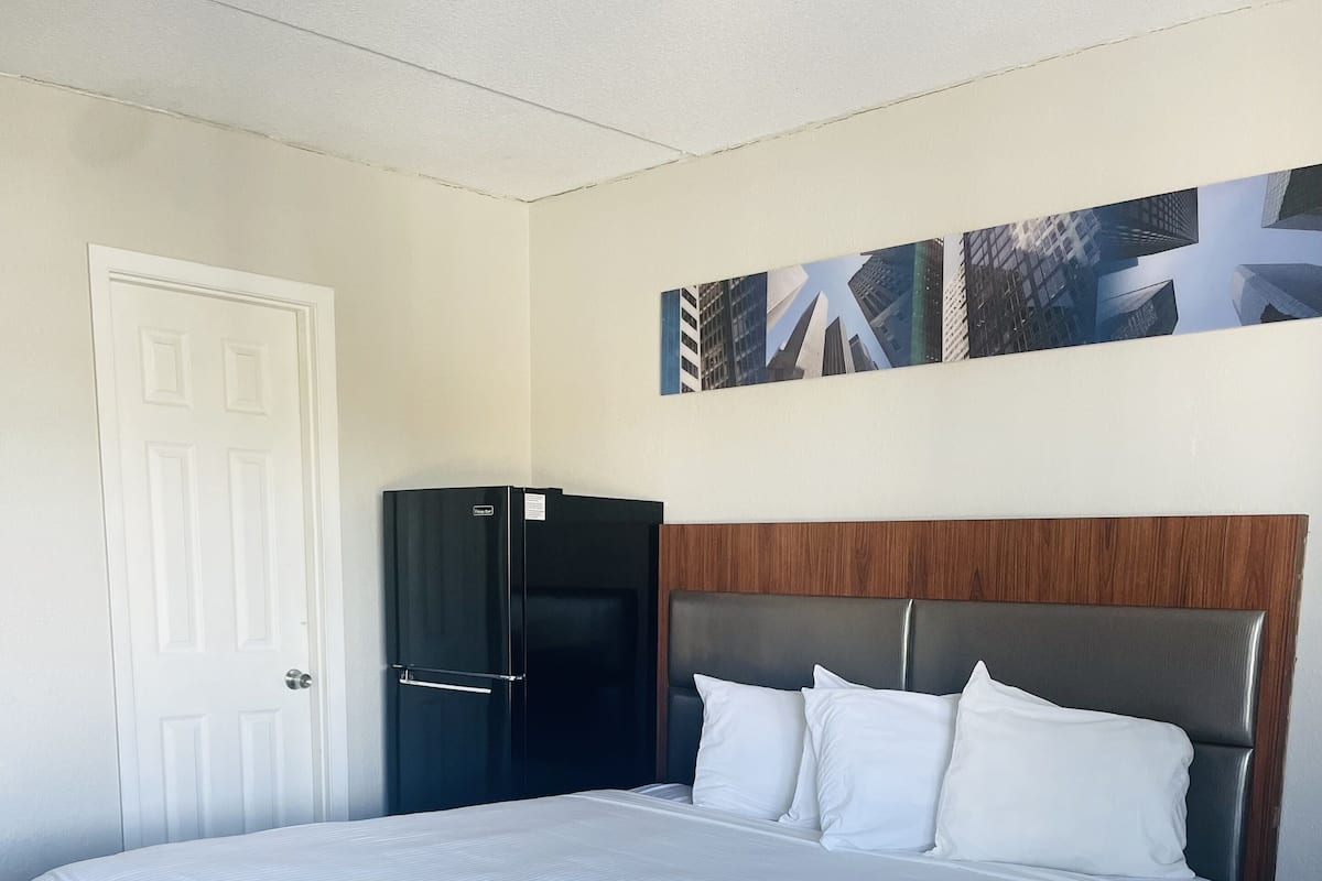 Una habitación de hotel con una cama grande, un cabecero de madera, un refrigerador negro y una puerta.