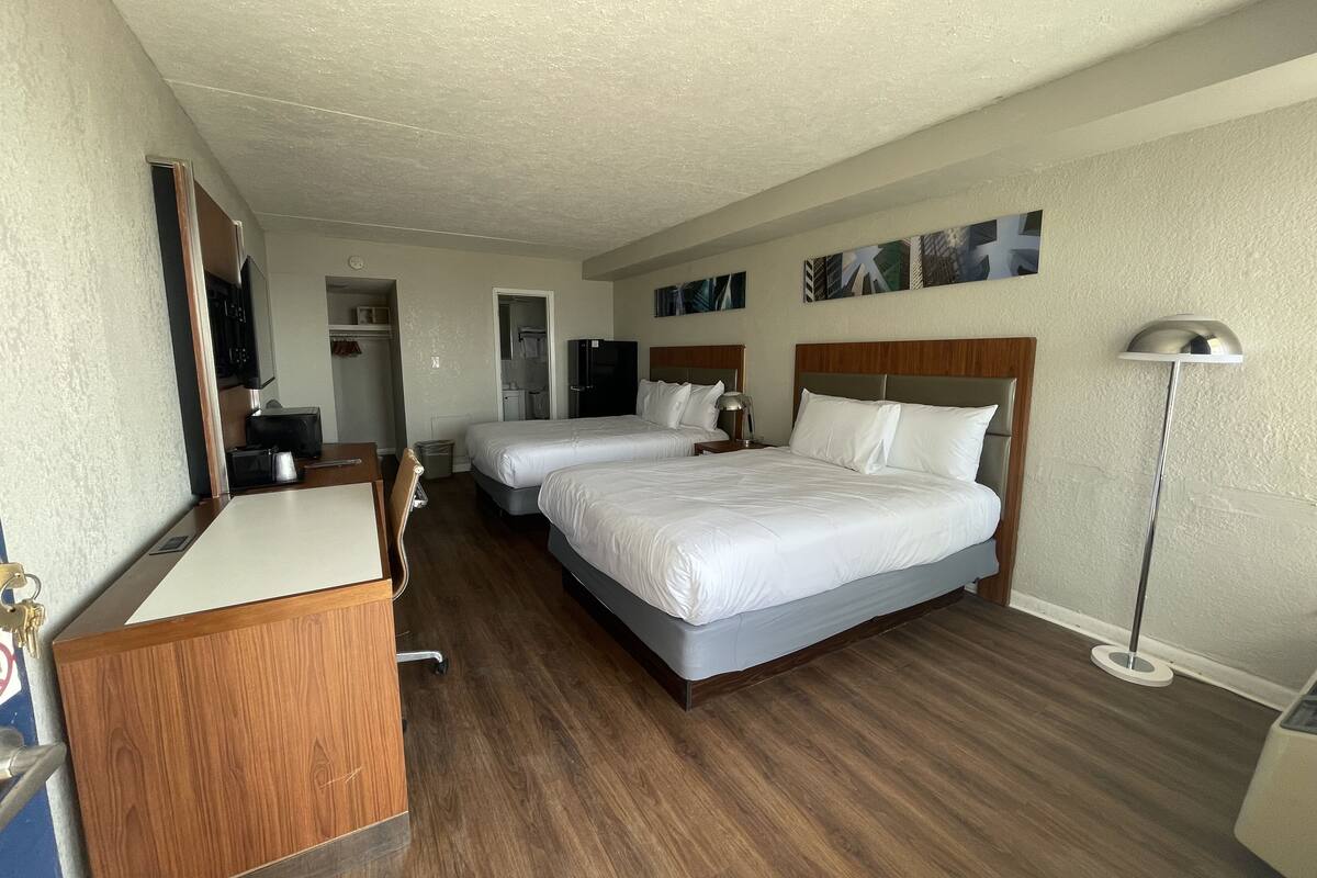 Una habitación de hotel con dos camas, un escritorio, un armario y un espejo.