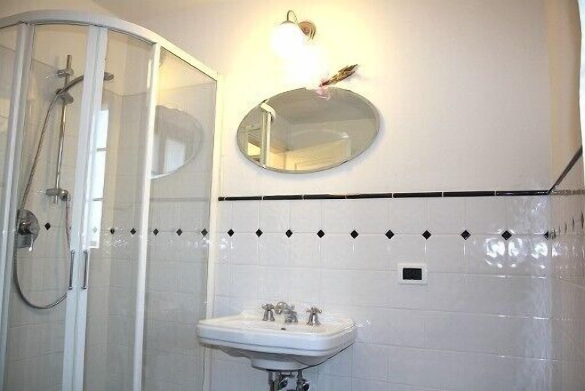 Une salle de bain avec une douche à parois de verre, un lavabo avec un miroir au-dessus et un mur carrelé agrémenté d’une bordure décorative.