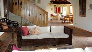 A cozy living room with a wicker sofa, a staircase, and a dining area in the background. - Agriturismo Ca' Lealtà (Caorle)