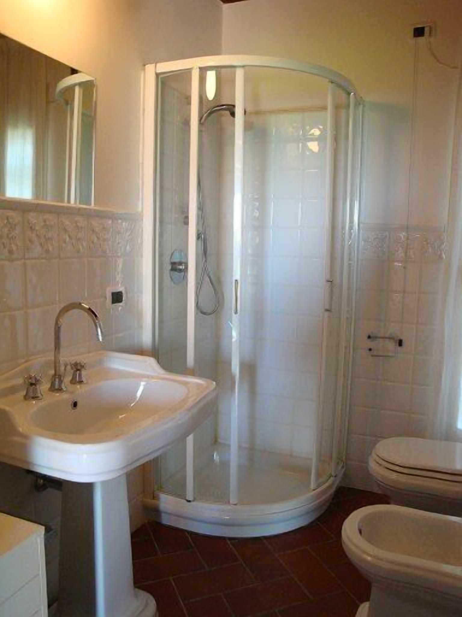 A bathroom with a glass-enclosed shower, a pedestal sink, and a toilet.