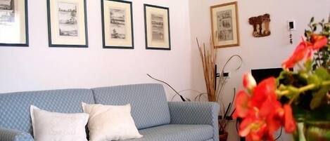 A room with a blue sofa, white cushions, and framed artwork on the wall.
