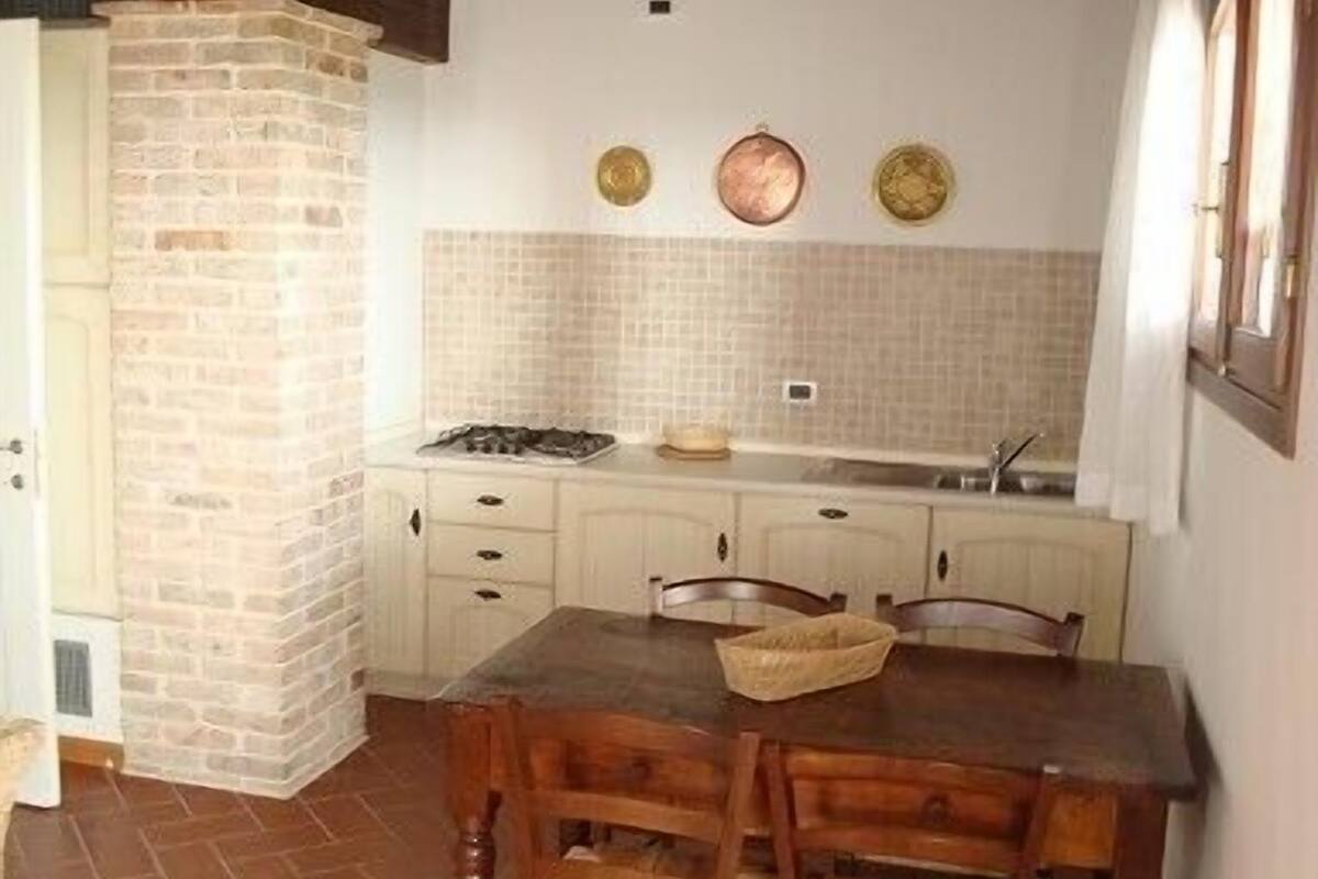 Une cuisine rustique avec un mur en pierre, des armoires blanches et une table à manger en bois, accompagnée de chaises.