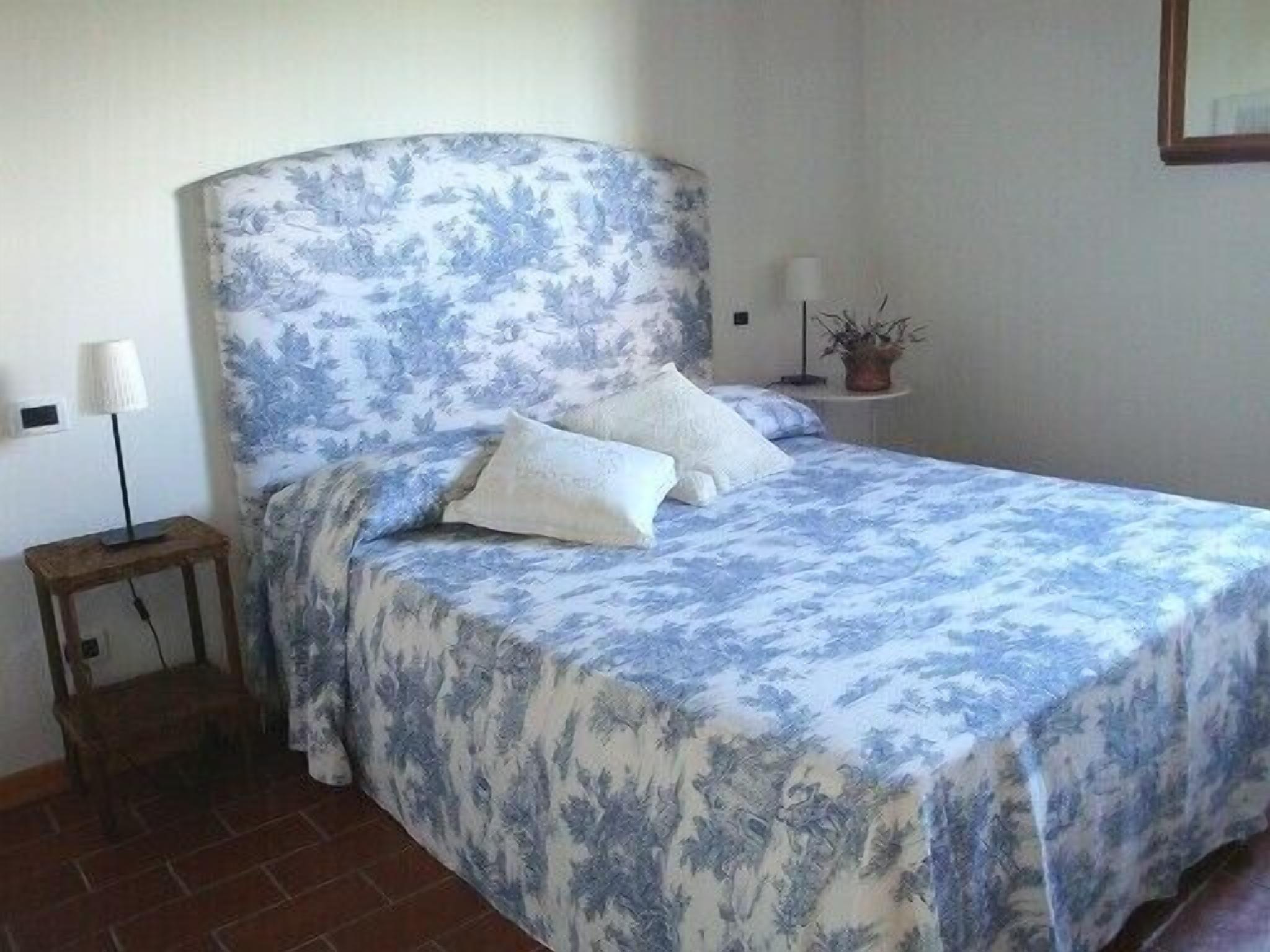 Un dormitorio con cama, mesita de noche, lámpara y planta en maceta.