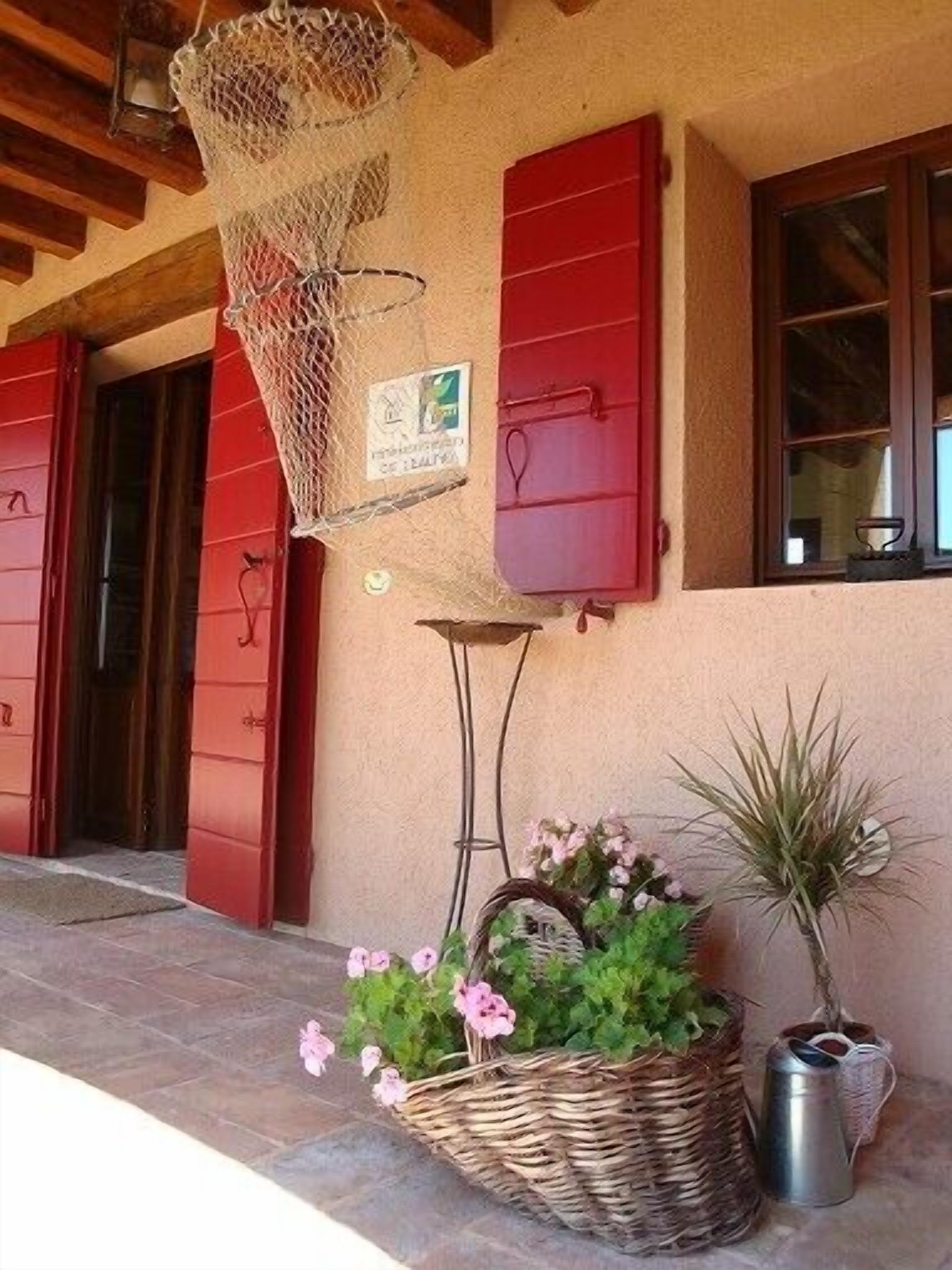 A building with red shutters, a wicker basket with flowers, and a metal watering can.