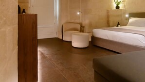 A stone-walled room with a bed, a wooden cabinet, and a small plant. - Le Malve Cave Retreat (Matera)