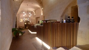 A reception area with a wooden reception desk, potted plants, and a modern chandelier. - Le Malve Cave Retreat (Matera)