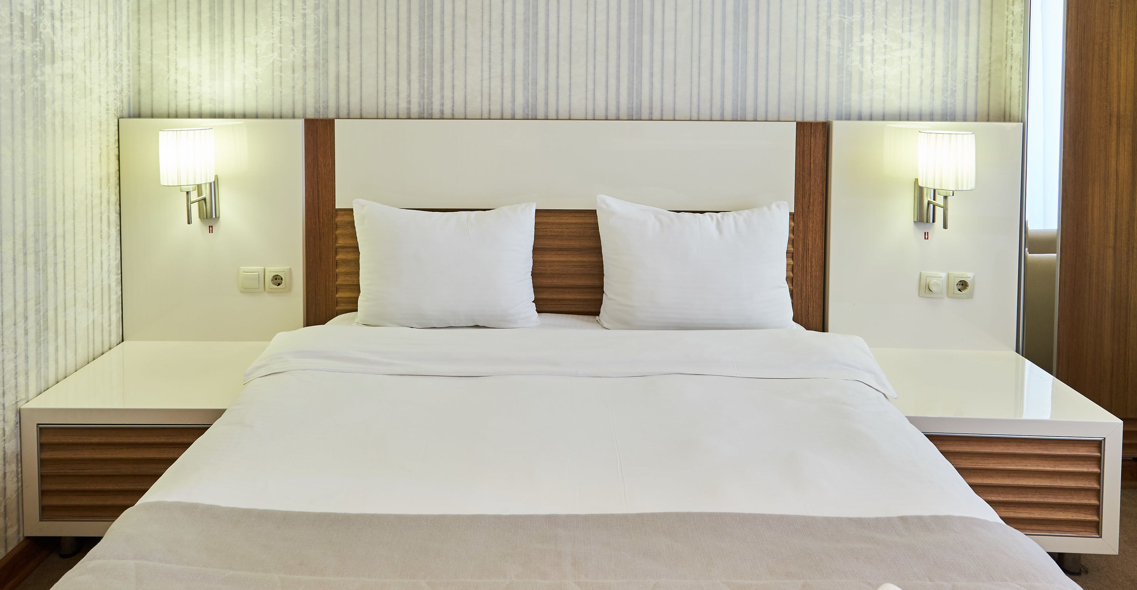 A hotel room with a large bed, two bedside lamps, and a wooden headboard.