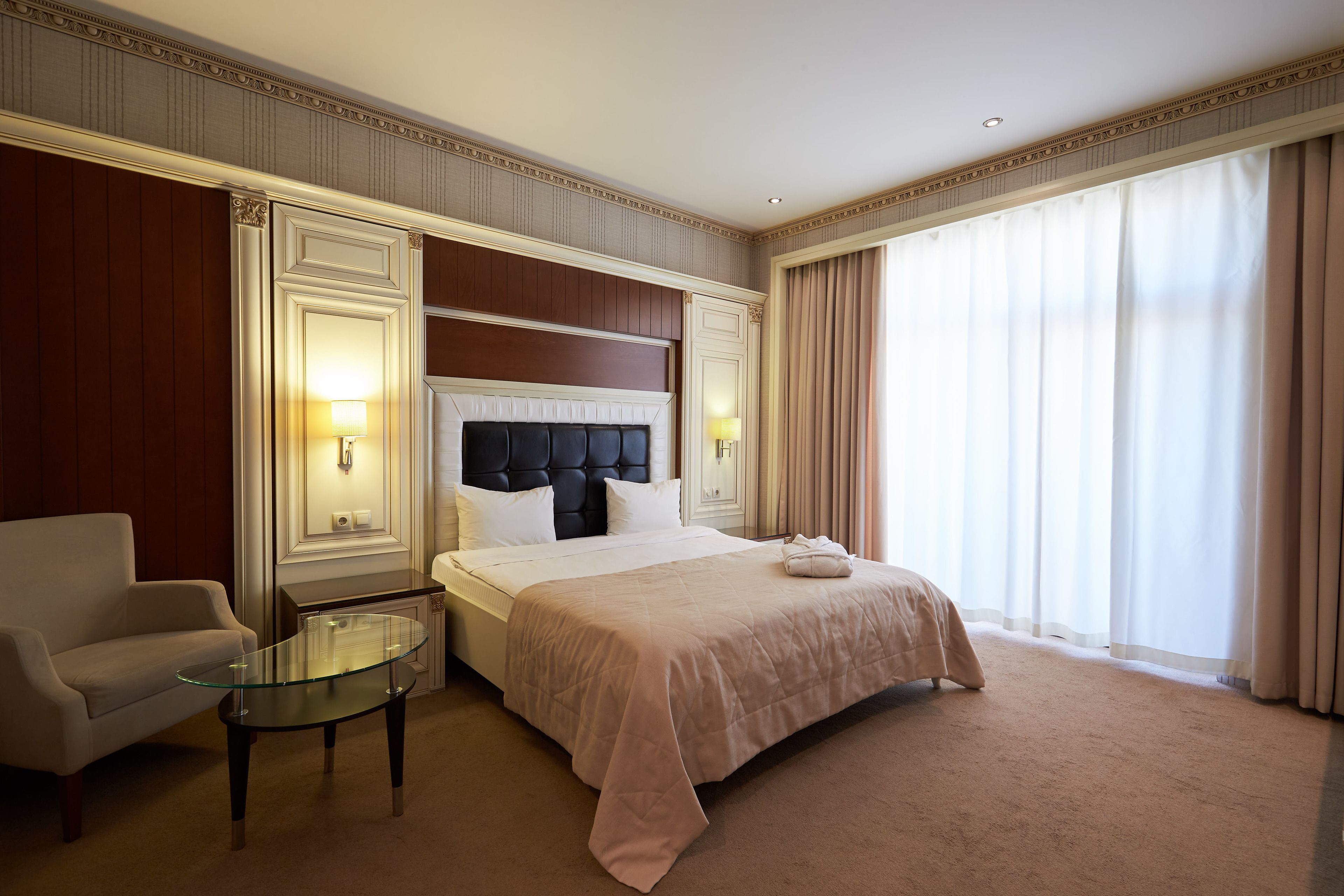 Ein Hotelzimmer mit einem großen Bett, einem Glastisch, einer Couch und Blick ins Freie durch große Fenster.