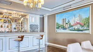 Een bar met een witte toog, meerdere barkrukken en een groot schilderij van een gebouw en bomen aan de muur.
