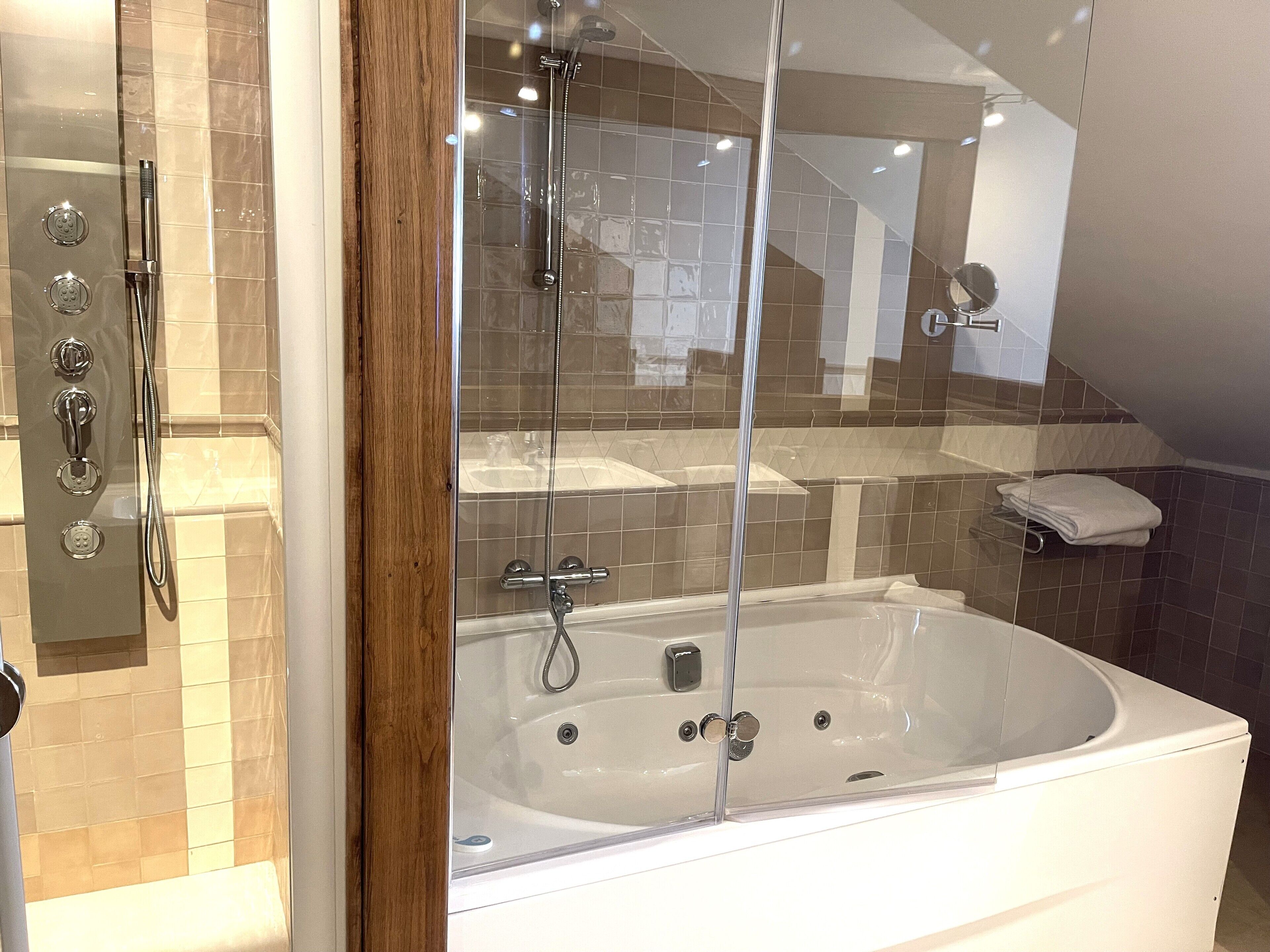 Un baño moderno con ducha de vidrio, bañera blanca y pared con azulejos.
