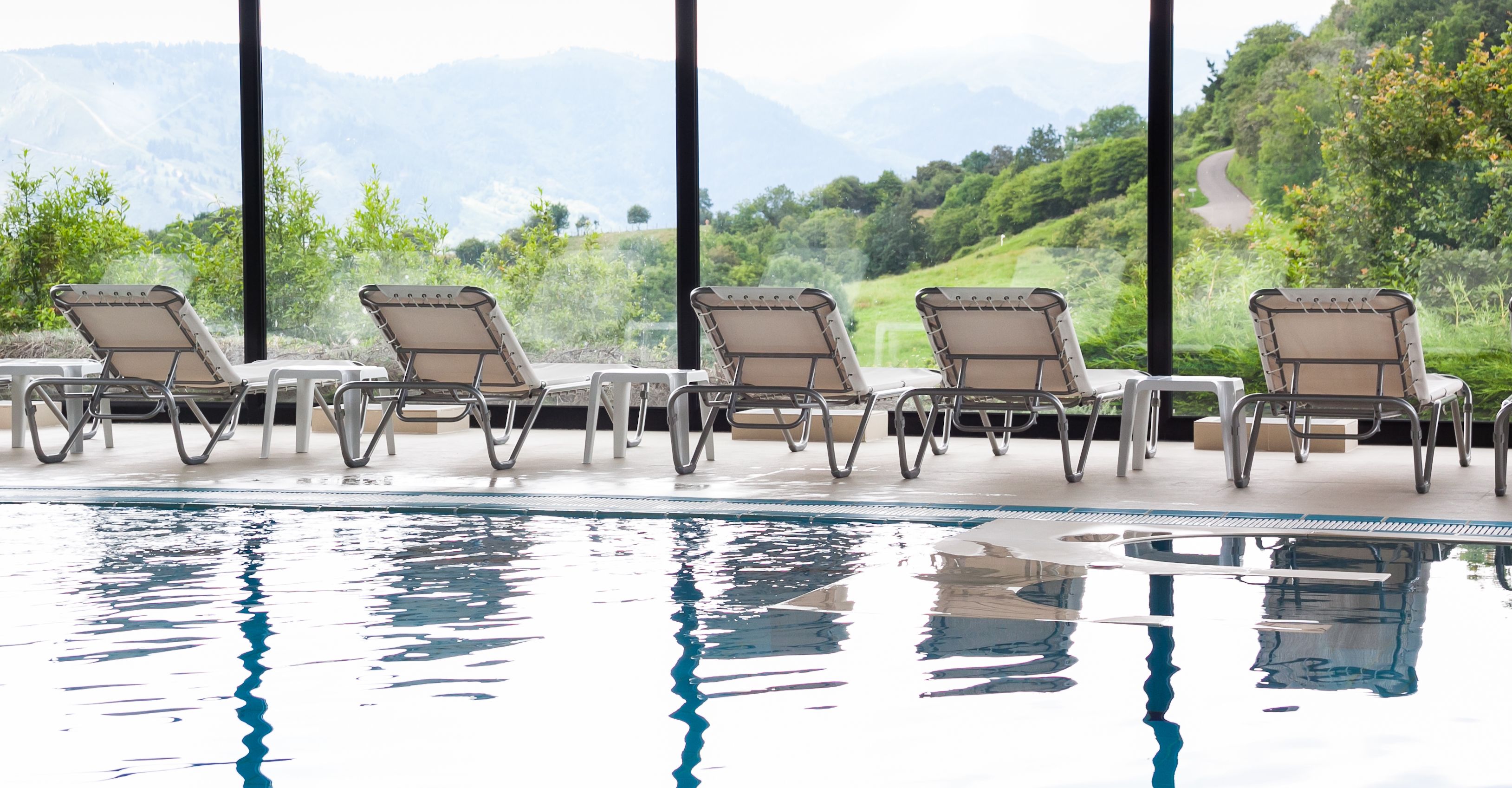 Zona junto a la piscina con sillones de descanso y vistas a un paisaje montañoso.