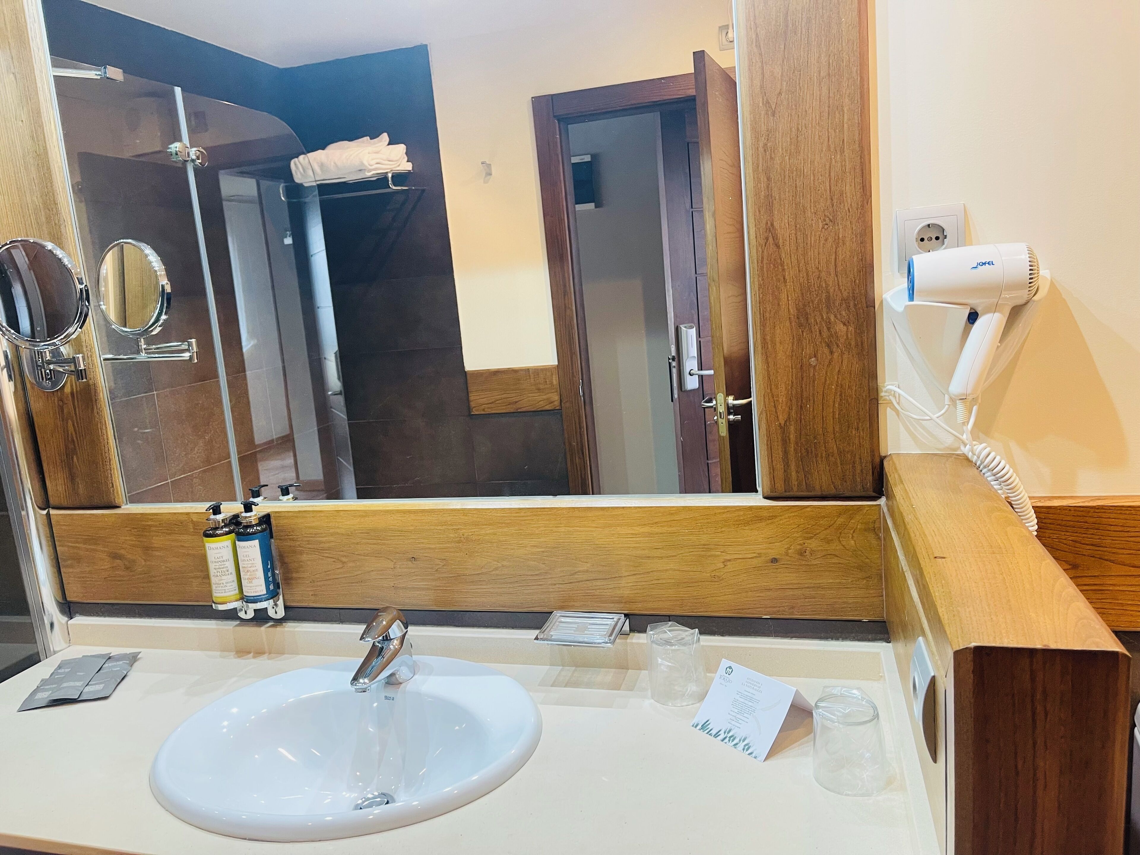 A hotel bathroom with a large mirror, a sink, a hairdryer, and toiletries.