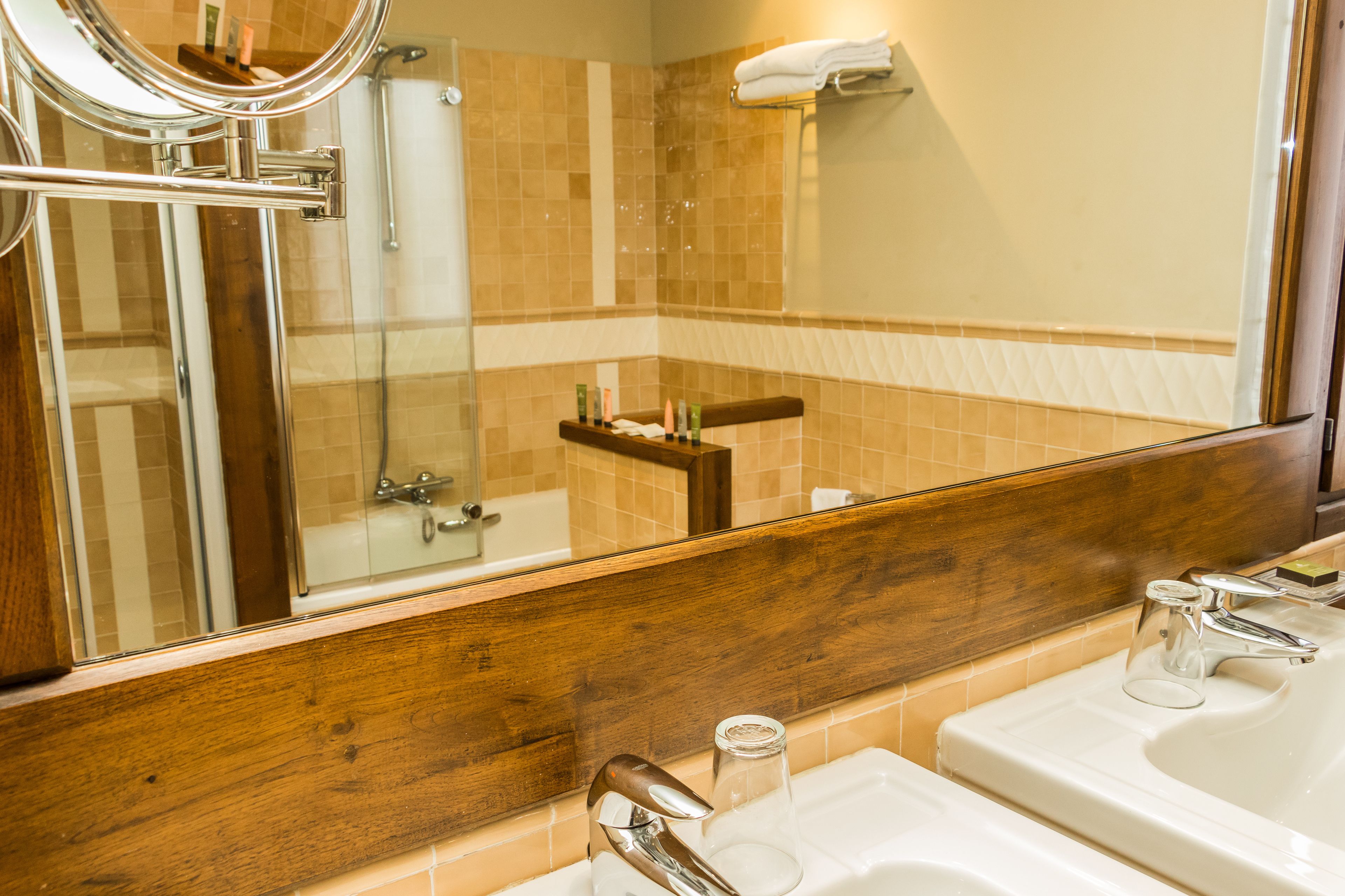 A bathroom with a large mirror, a glass shower enclosure, and a sink with a glass.
