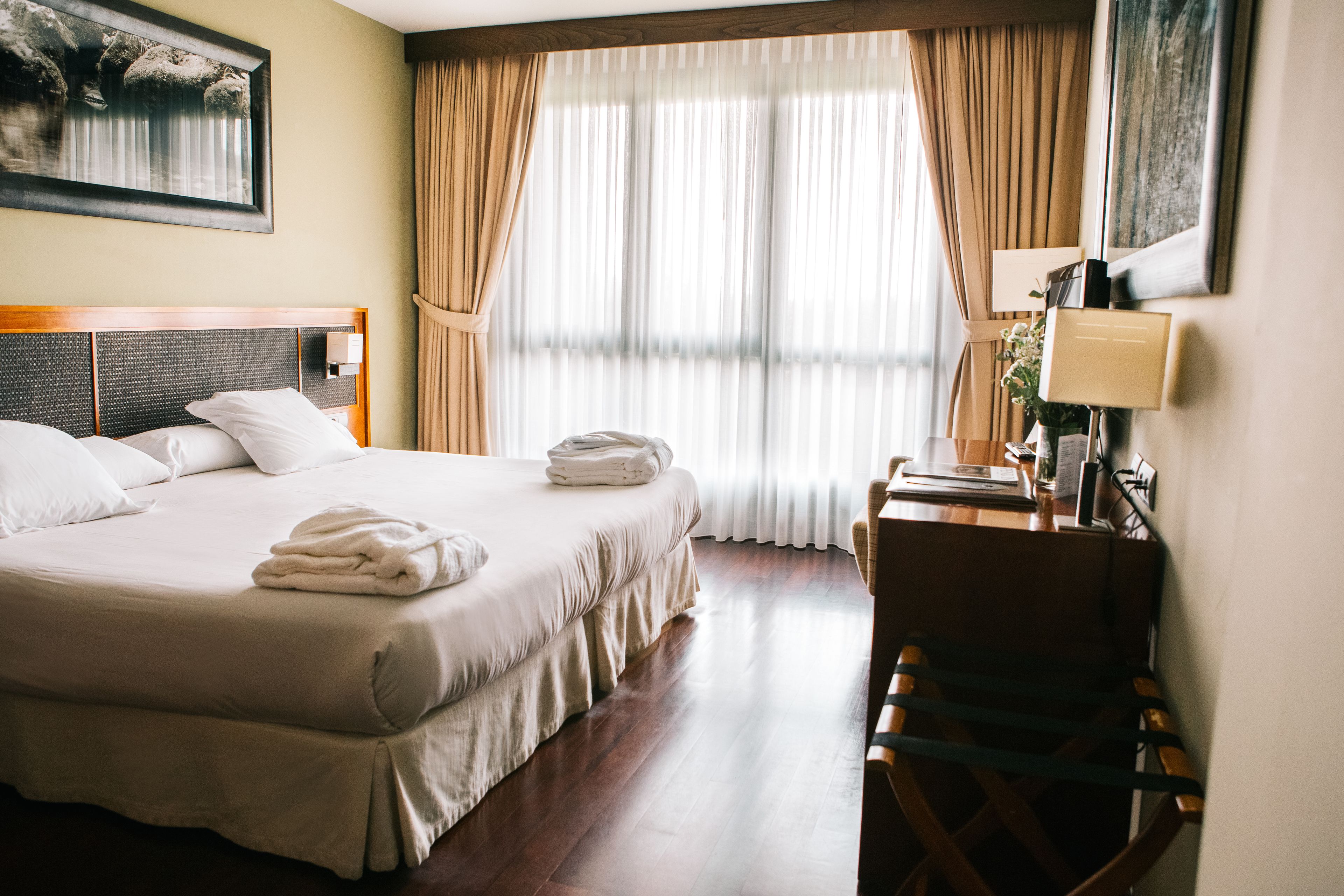 A hotel room with a large bed, a desk, a chair, and a window with curtains.