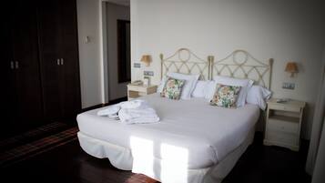 Una cama bien hecha con sábanas blancas y almohadillas florales, una mesita de noche con lámpara y un armario de madera oscura en una habitación de hotel.