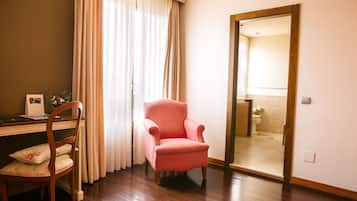 Una habitación con un escritorio de madera, un sillón rosa y una silla de madera con cojín floral.