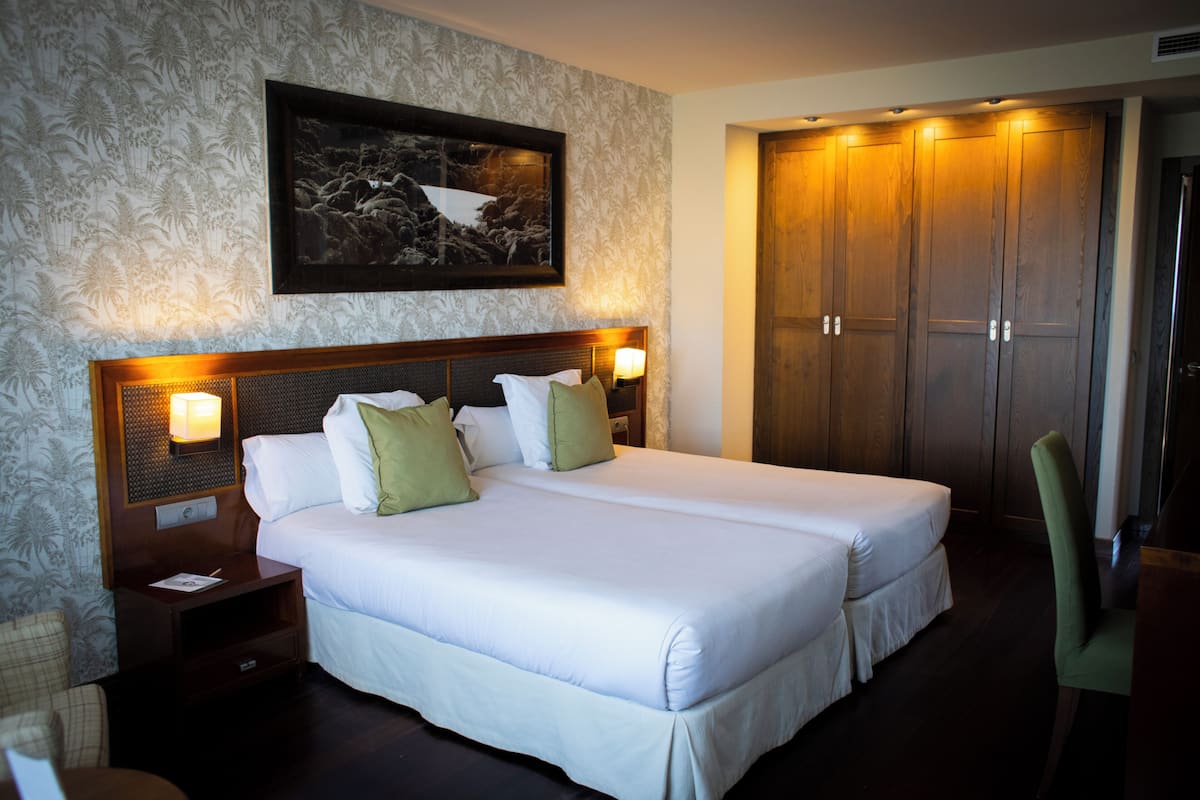 Une chambre d’hôtel avec deux lits, un grand tableau encadré au mur et une armoire en bois.